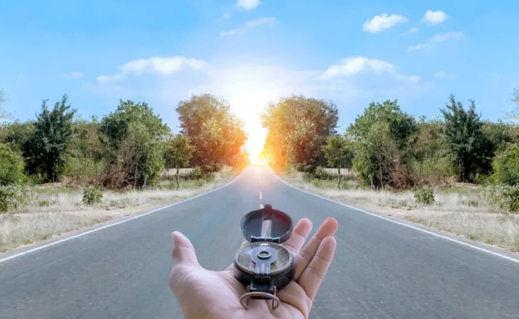 Mano sosteniendo una brújula en una carretera al amanecer, símbolo de orientación y claridad para dar el siguiente paso en tu carrera o negocio después de los 40.