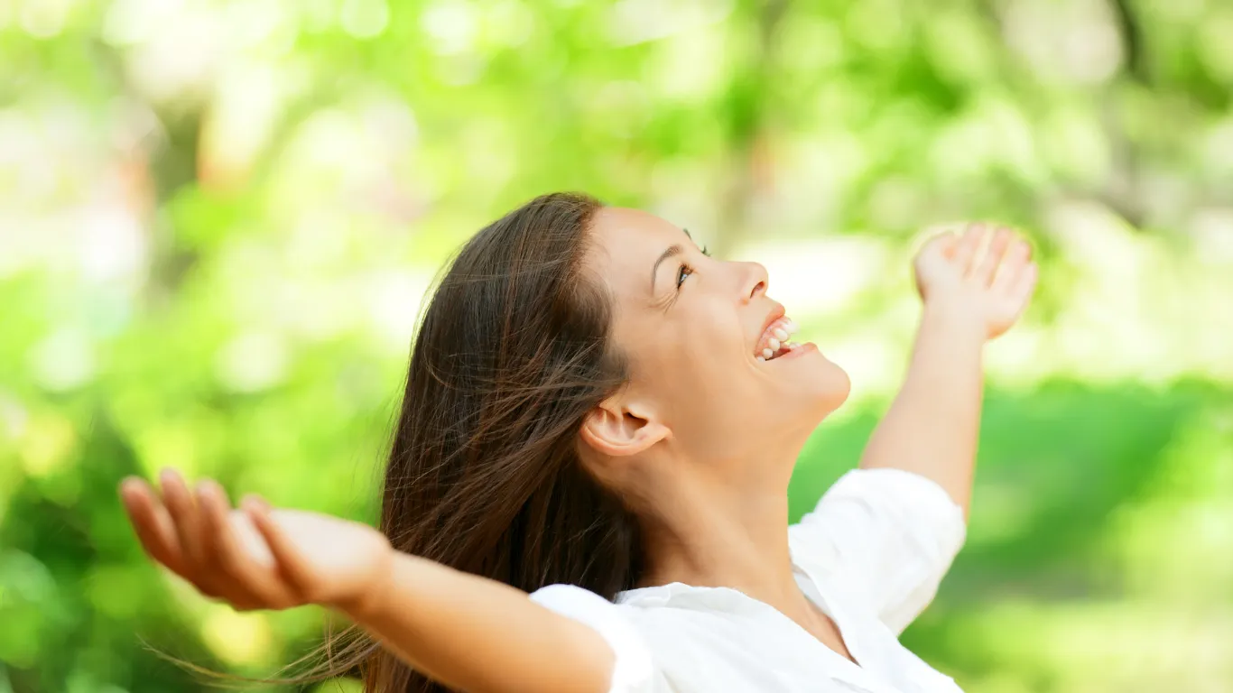 Mujer sonriente al aire libre, sintiéndose libre y en paz después de reducir el estrés con el programa Oxigénate para el manejo del estrés profesional.