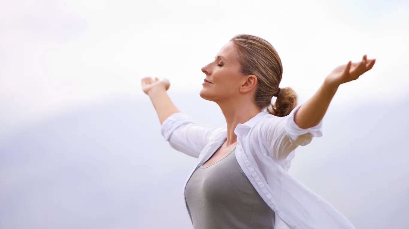 Mujer con los brazos abiertos en la naturaleza, disfrutando del equilibrio y la paz interior después de reducir el estrés con el programa Oxigénate.